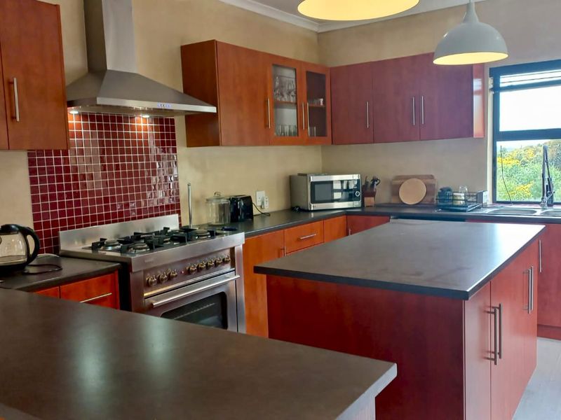 A functional kitchen featuring wooden cabinetry, a gas stove with extractor fan, a central island, and a tiled backsplash with a window view.
