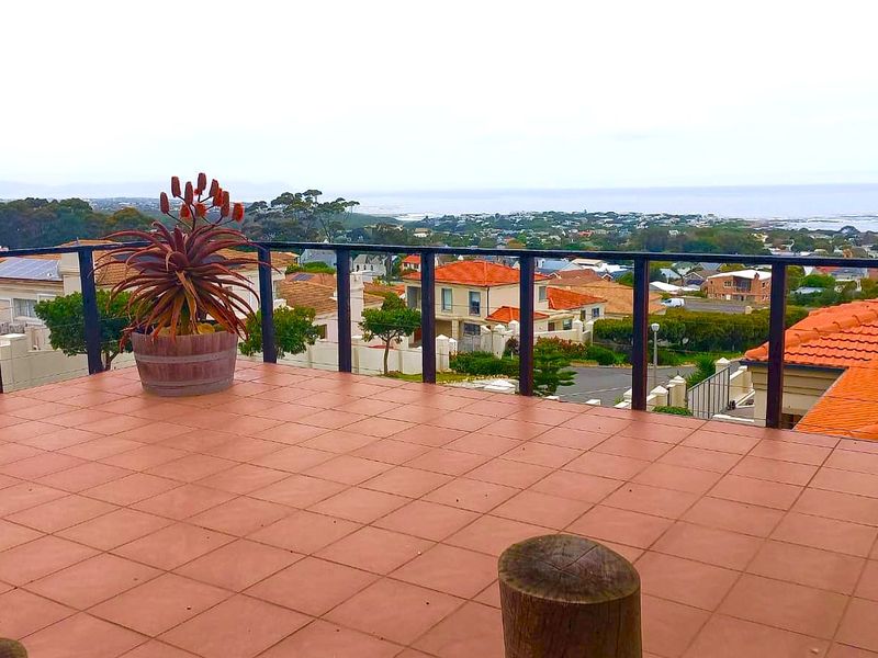 An elevated balcony featuring tiled flooring and a metal balustrade, offering expansive views over the surrounding residential area and coastline.