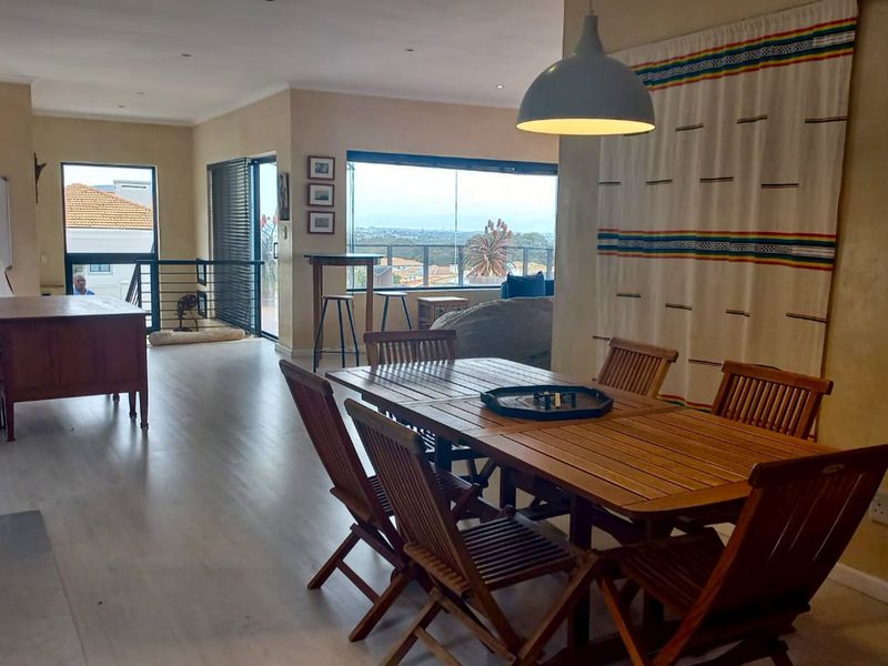 Spacious open-plan living and dining area featuring laminate flooring, recessed lighting, and large glass doors leading to an outdoor balcony with scenic views.