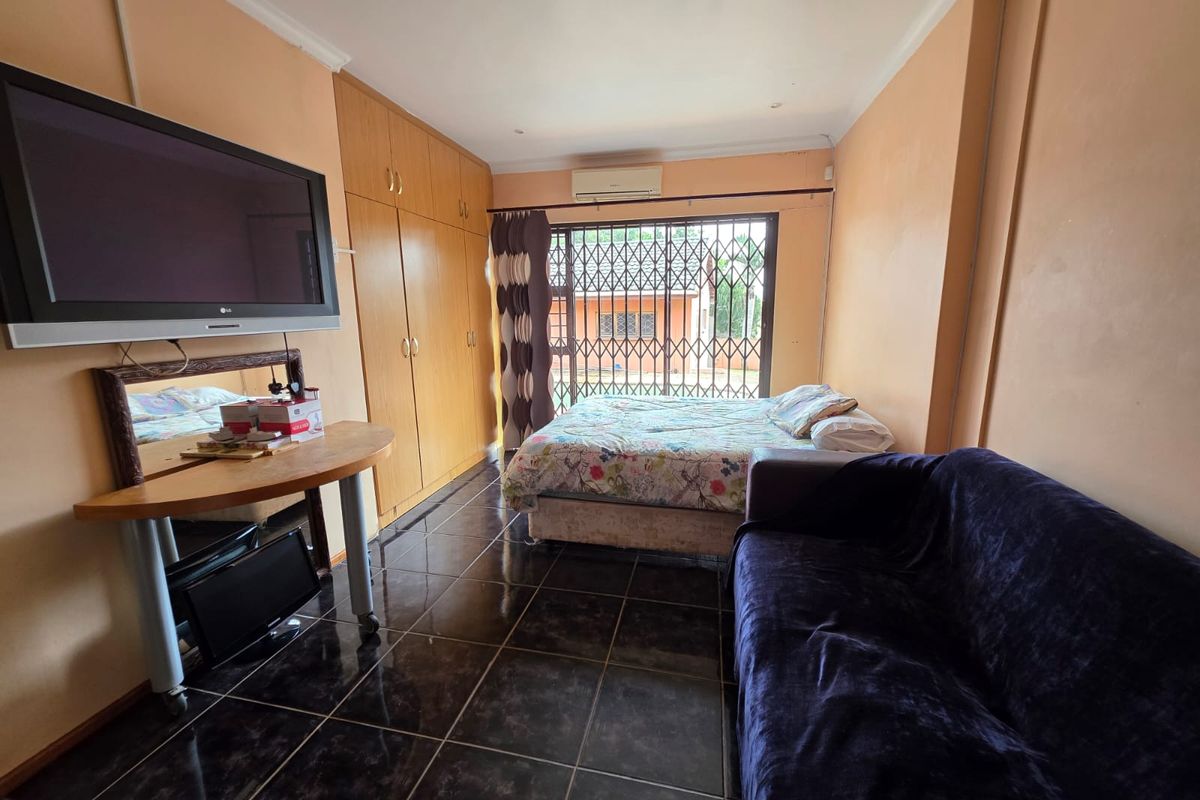 A bedroom featuring built-in cupboards, tiled flooring, and a wall-mounted air conditioning unit, with access to an exterior area via a security gate.