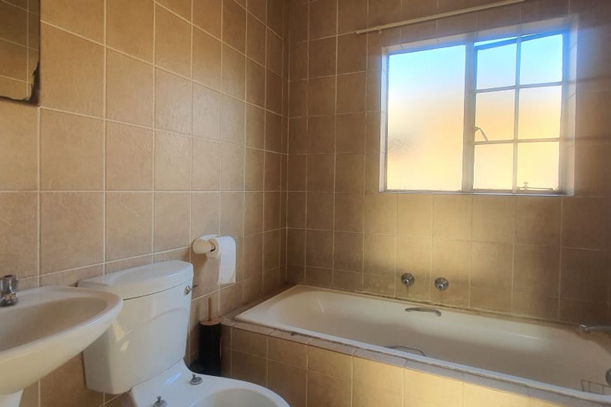 A dated bathroom featuring full-height wall tiling, a built-in bathtub, pedestal basin, and toilet, requiring cosmetic updates to modernize the space.