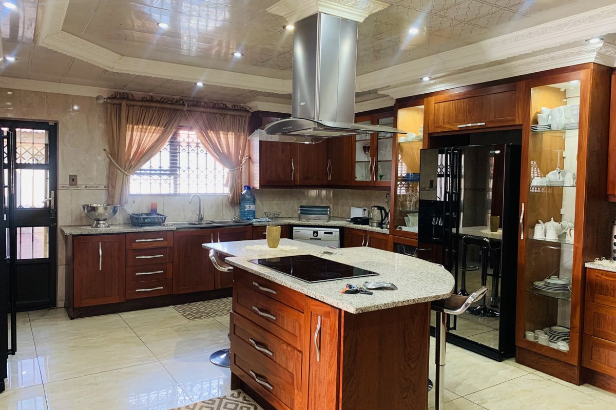 Spacious kitchen featuring rich wood cabinetry, granite countertops, a central island with an integrated hob, and a decorative coffered ceiling with recessed lighting.