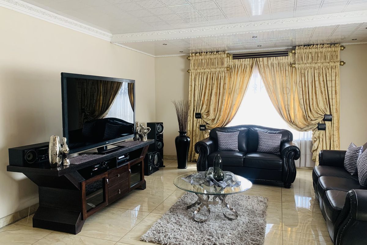 A well-maintained living room featuring polished floor tiles, decorative ceiling panels with crown molding, and recessed lighting.
