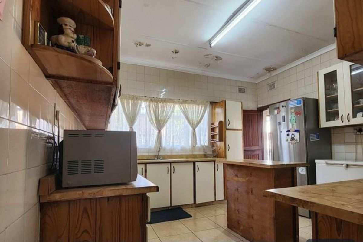 A dated kitchen featuring wooden cabinetry, tiled backsplash, and tiled flooring, currently showing signs of ceiling water damage and wear.