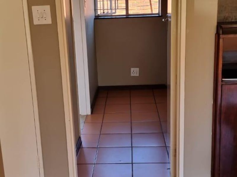 A tiled hallway leading to a small room with a window, featuring a built-in cupboard and visible floor tile damage.