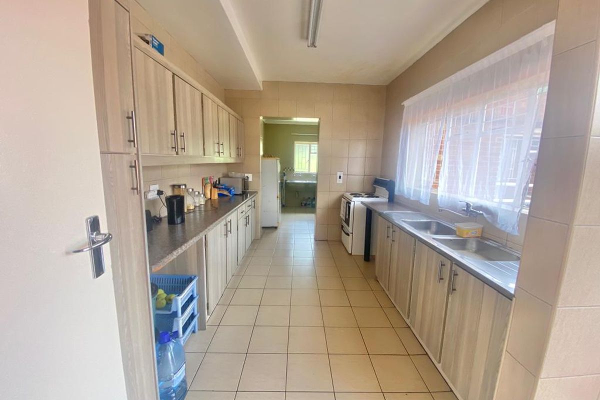 Functional kitchen featuring laminate cabinetry, tiled surfaces, and a double basin sink, with an adjacent scullery area visible through the doorway.