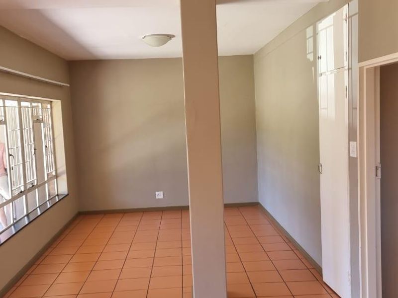 An empty living area featuring tiled flooring, a structural support column, and windows fitted with security bars.