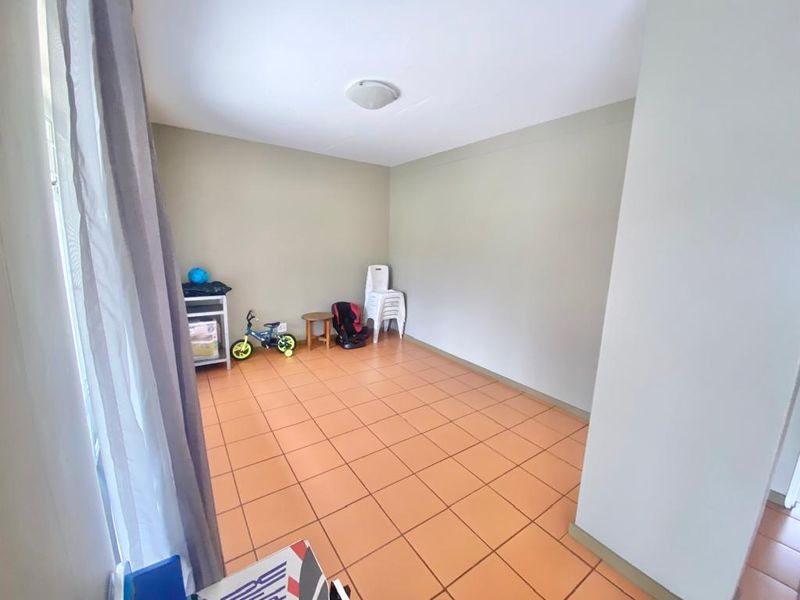 A spacious, neutral-toned living area featuring ceramic tile flooring and a simple flush mount ceiling light, offering a blank canvas for interior design.