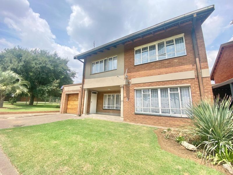 A two-story brick townhouse featuring a paved driveway, integrated garage, and secure window treatments, set within a well-maintained front garden.