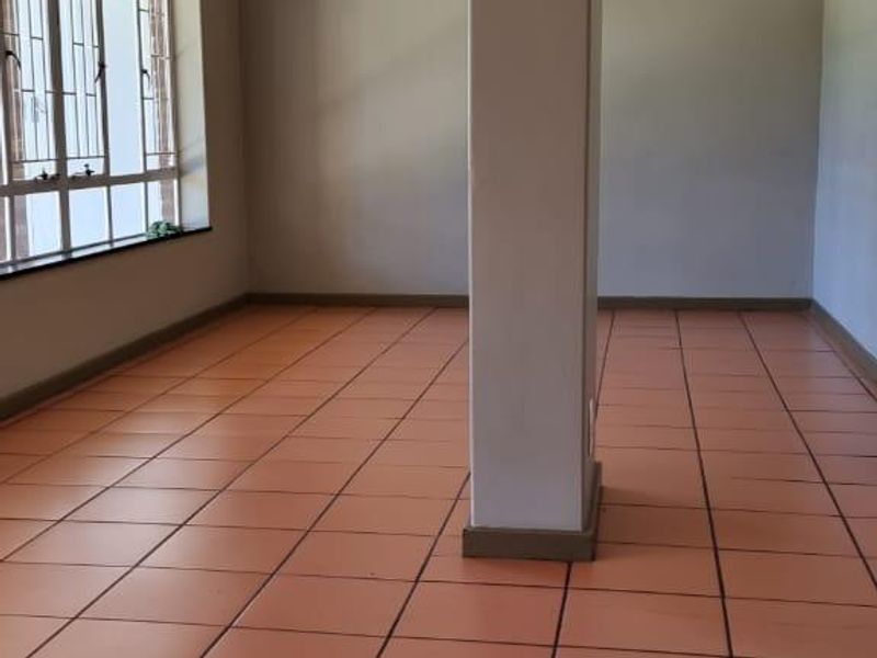 An empty living area featuring ceramic floor tiles, a central structural support column, and large windows with security bars.