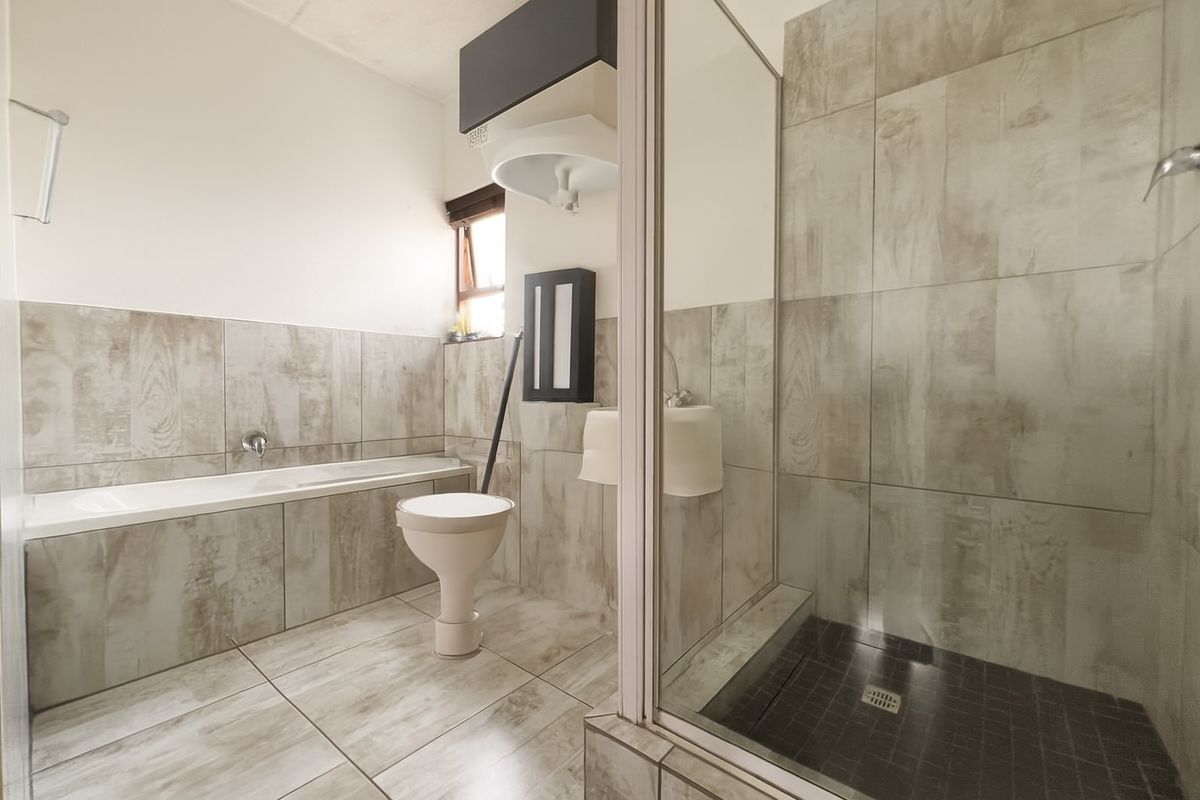 A functional bathroom featuring a built-in bathtub, a separate glass-enclosed shower, and neutral wood-look wall tiling throughout.