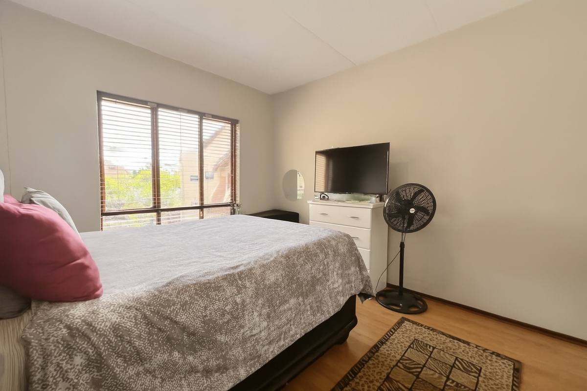 A bedroom featuring laminate flooring and large windows with fitted blinds, providing natural light.