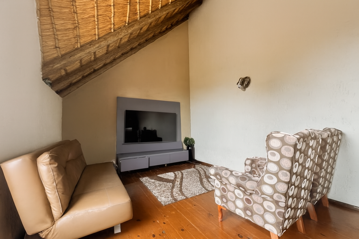 A cozy living room featuring a unique raked thatched ceiling, timber flooring, and a built-in media console unit.