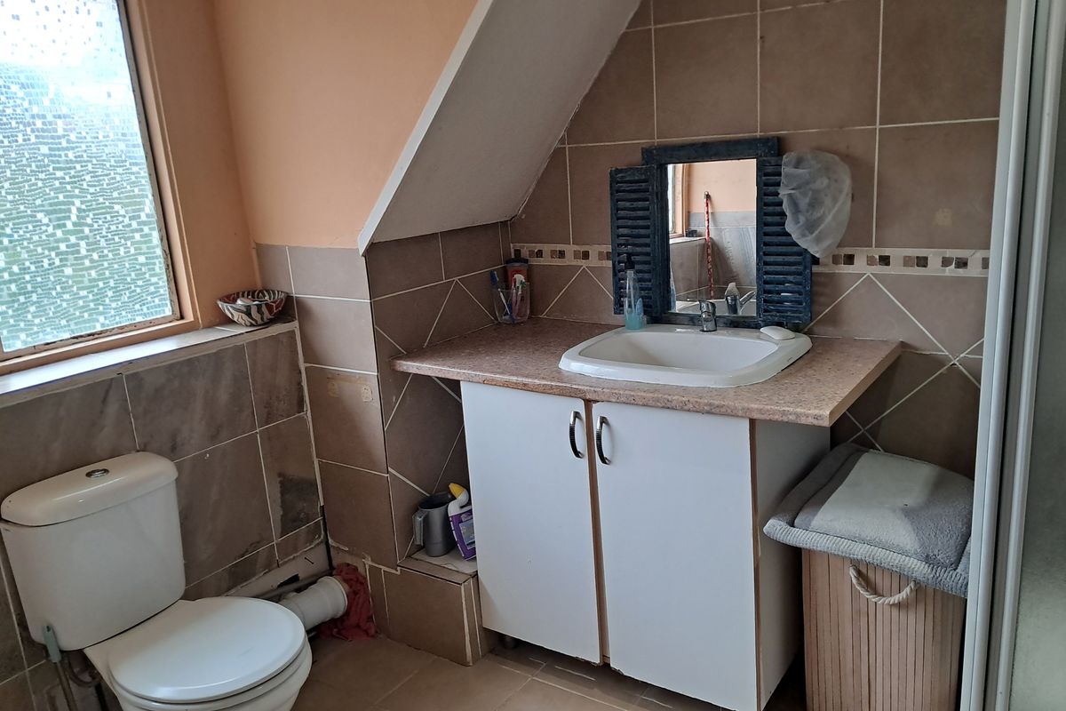 A compact bathroom featuring a vanity unit with basin, toilet, and tiled walls under a sloped ceiling, requiring cosmetic updates and maintenance.