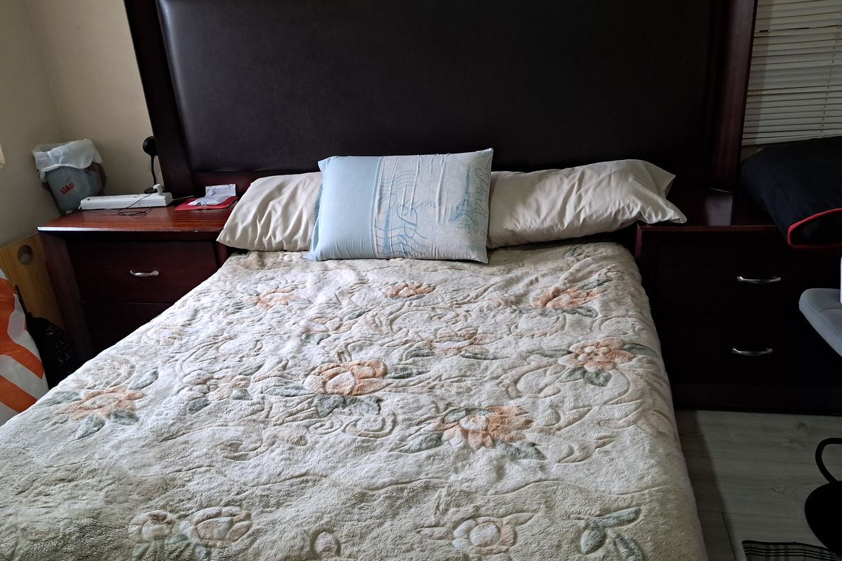 A bedroom featuring a large built-in headboard with integrated bedside cabinetry and light-toned laminate flooring.