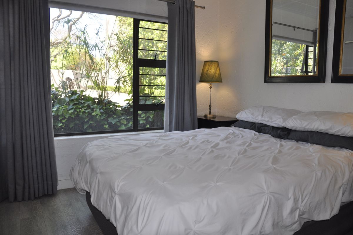A bedroom featuring large windows with garden views, neutral wall finishes, and wood-look flooring.