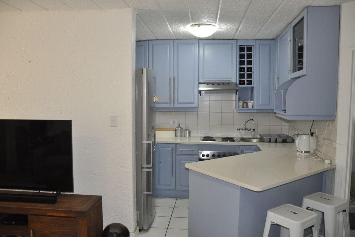 Compact kitchen featuring blue cabinetry, tiled backsplash, built-in hob, extractor fan, and a breakfast bar counter, seamlessly integrated with the living area.