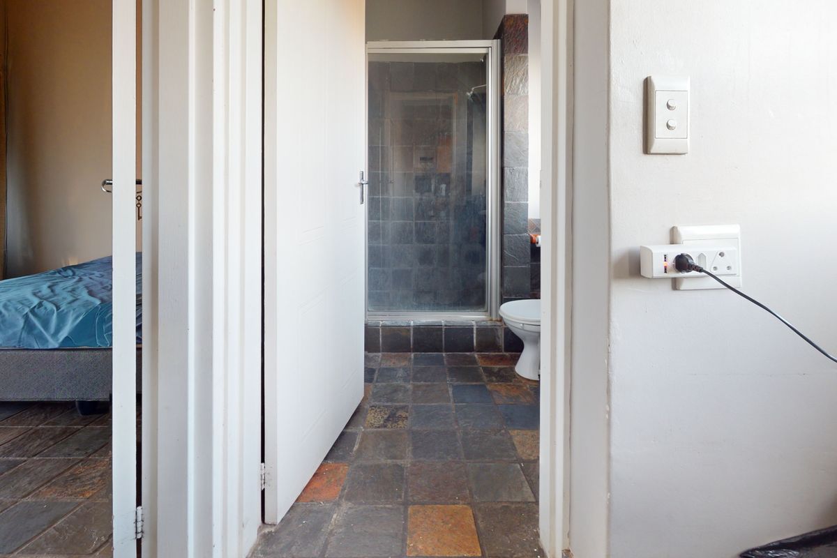 A view from a hallway into a bathroom featuring slate floor tiles, a shower enclosure, and a toilet, adjacent to a bedroom.
