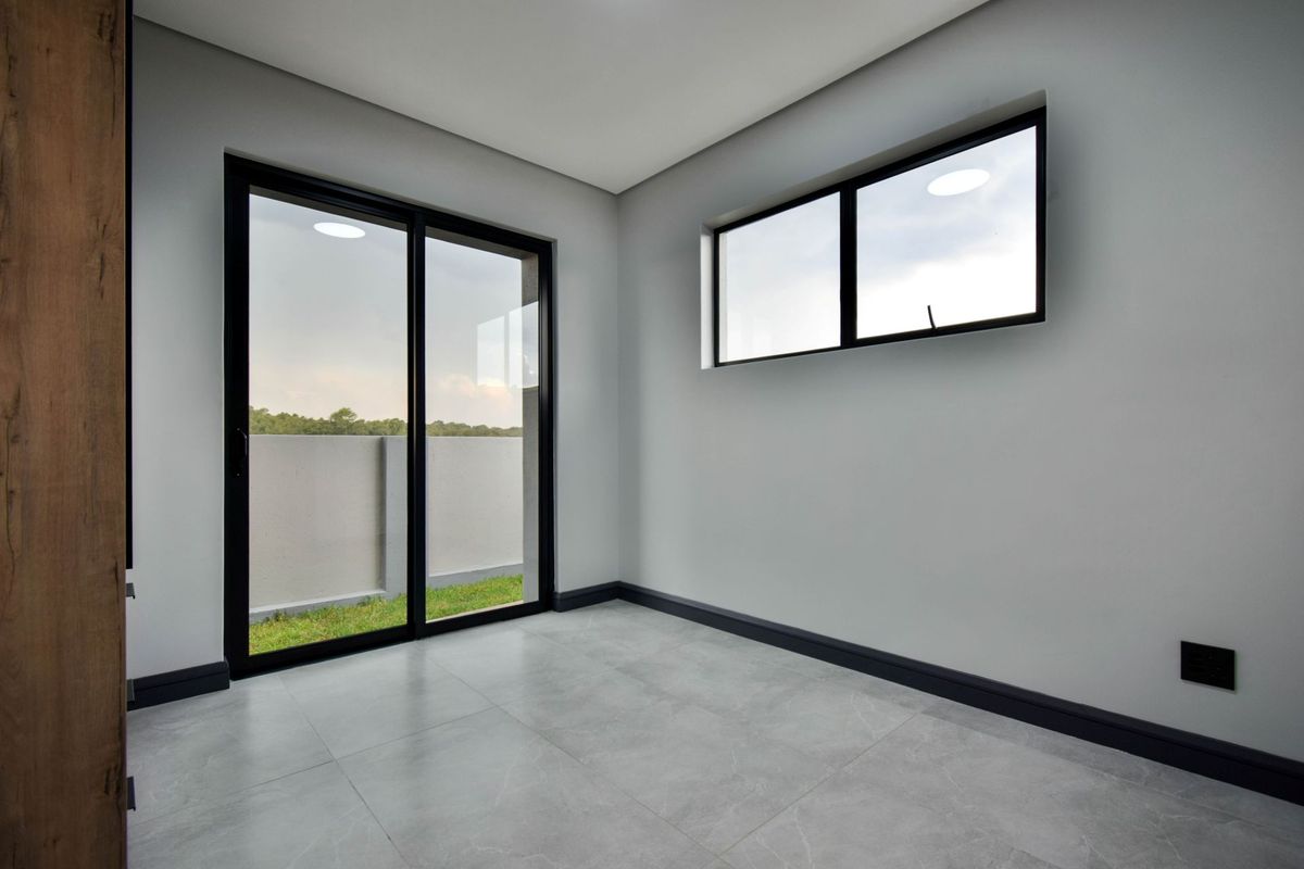 A bright, modern, and empty bedroom featuring large sliding glass doors, neutral grey tiled flooring, and contemporary black window frames.