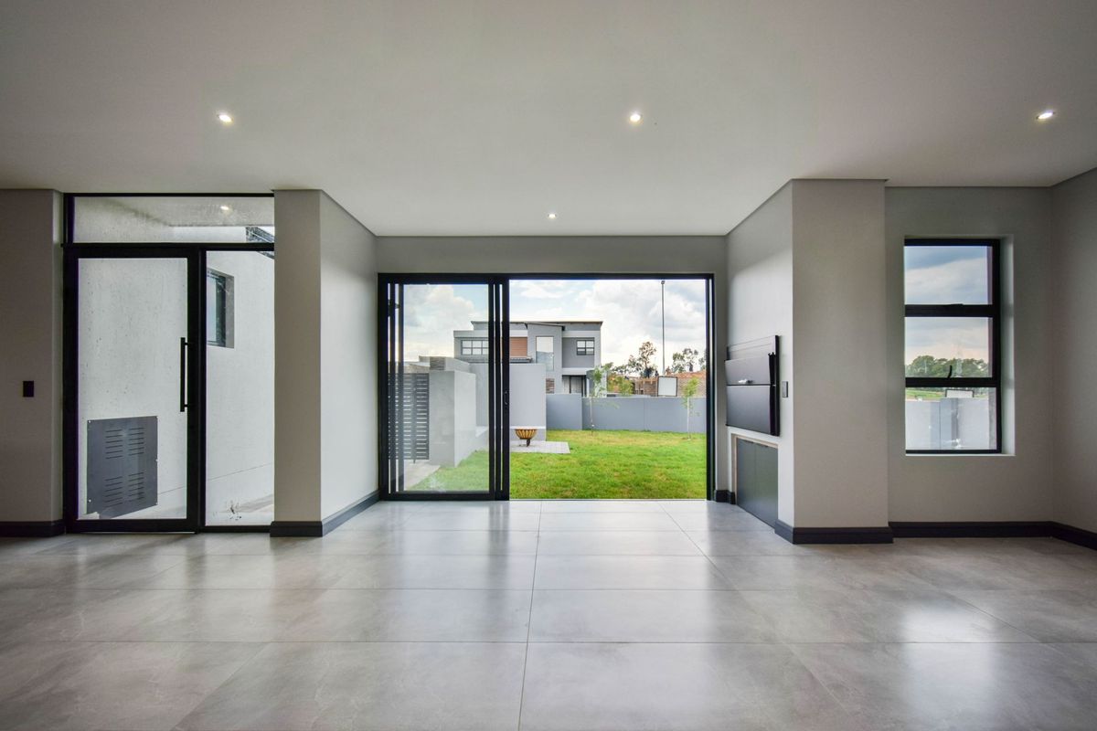 Spacious, modern living area featuring large format floor tiles, recessed lighting, and seamless access to the rear garden through black aluminium sliding doors.
