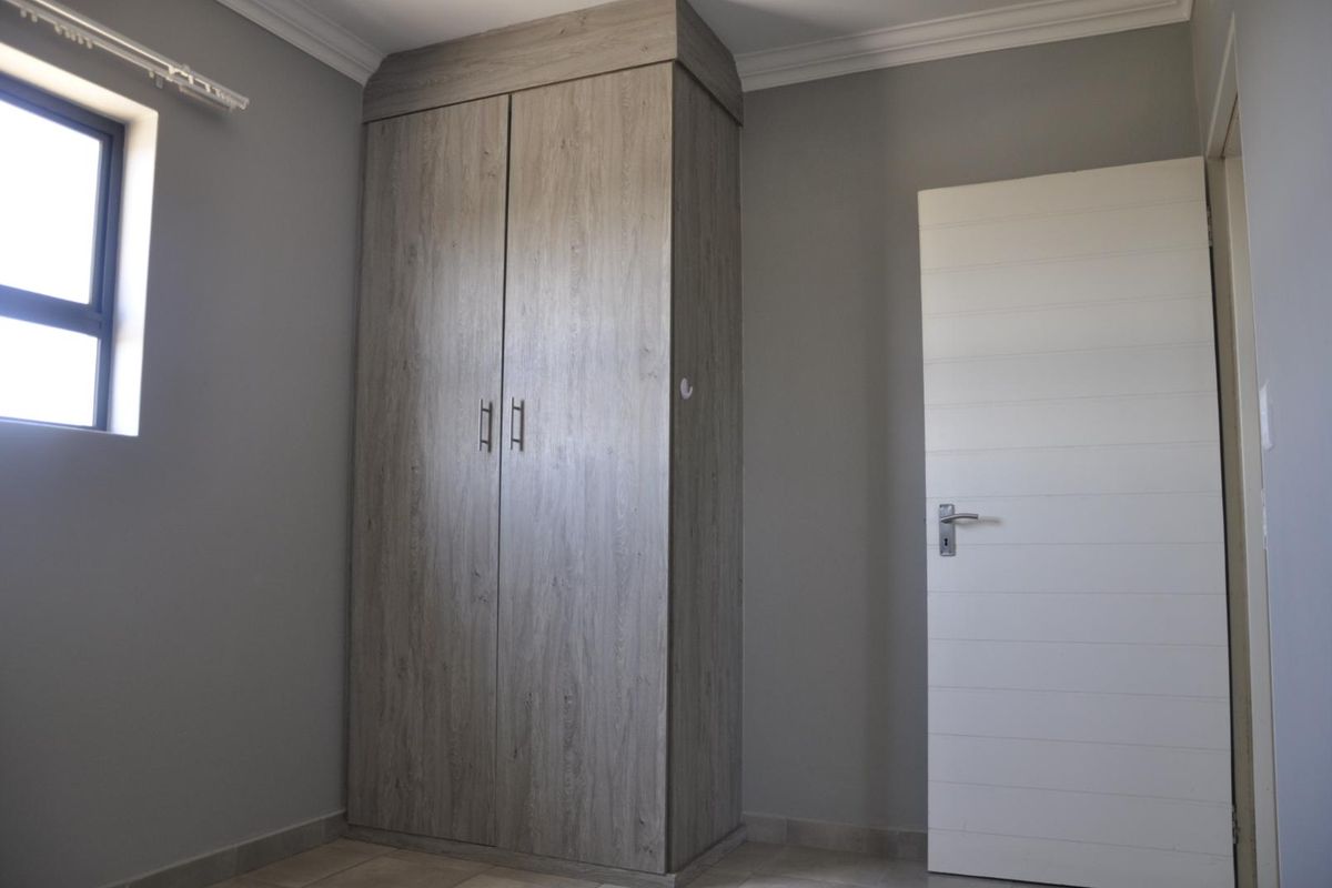 A bedroom featuring a built-in wooden wardrobe, neutral grey walls, tiled flooring, and a white interior door.