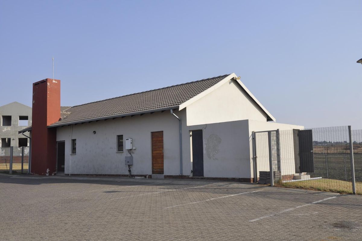 Exterior view of a single-story building featuring a tiled roof, paved parking area, and perimeter fencing.