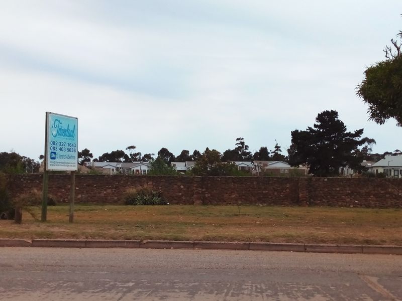 A vacant residential plot featuring a stone boundary wall and existing real estate signage, viewed from the street.