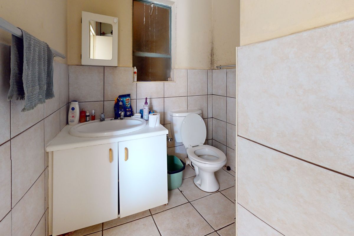 A compact bathroom featuring a vanity cabinet with basin, toilet, and tiled finishes, requiring cosmetic updates to address wall staining and dated fixtures.
