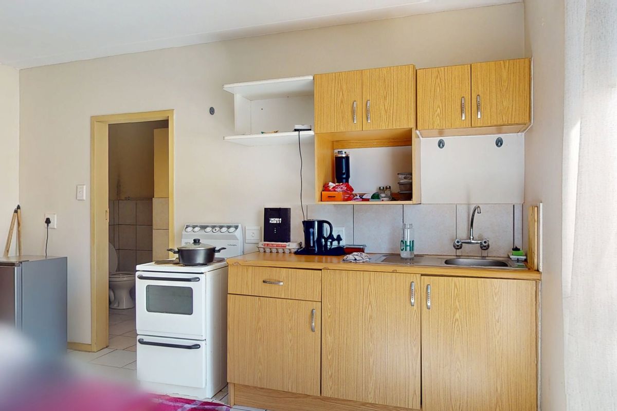 Compact kitchen featuring laminate cabinetry, a stainless steel sink, and a freestanding stove, with an adjacent view into the bathroom area.