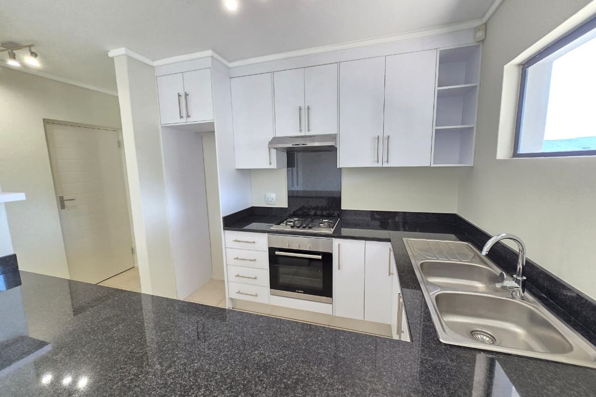 Modern kitchen featuring granite countertops, built-in oven, gas hob, extractor fan, and a double bowl stainless steel sink with ample cabinetry.
