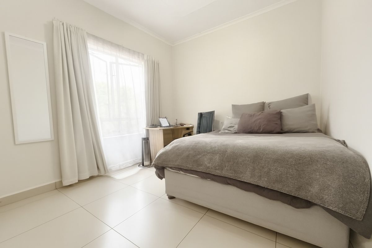 A bright bedroom featuring neutral tiled flooring, large windows with curtains, and a clean, minimalist layout suitable for comfortable living.