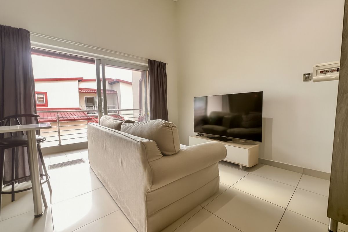 A bright living room featuring large sliding glass doors leading to a balcony, tiled flooring, and high ceilings.