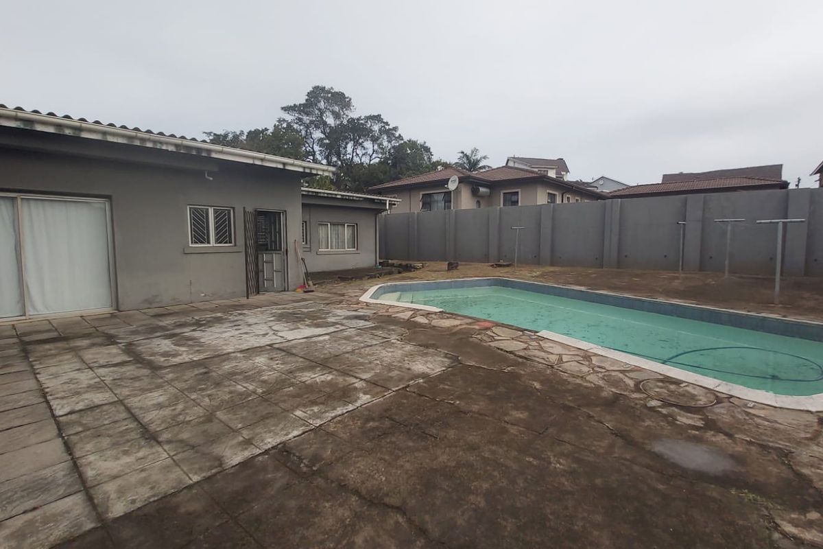 Rear exterior view featuring a swimming pool, paved patio area, and high perimeter wall, requiring maintenance and landscaping updates.