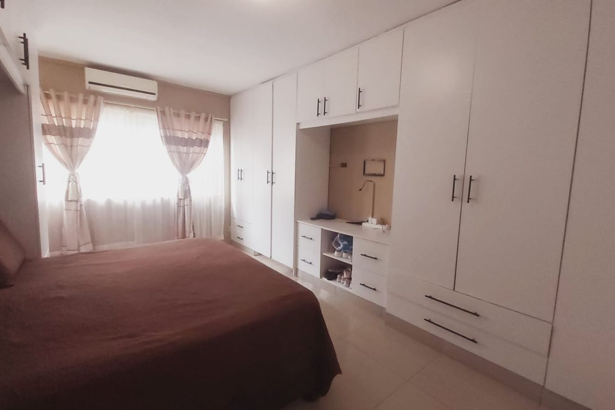 A well-maintained bedroom featuring extensive white built-in cabinetry, tiled flooring, and a wall-mounted split-system air conditioning unit.