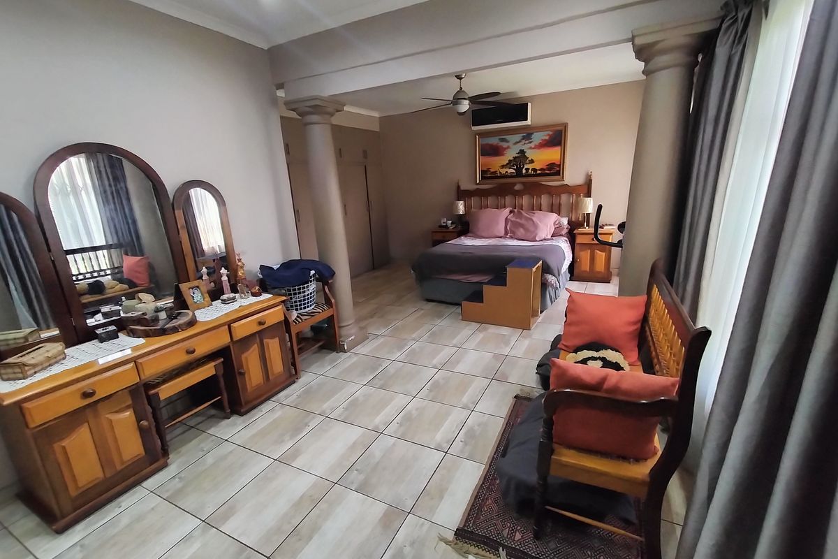 Spacious bedroom featuring tiled flooring, built-in cupboards, a ceiling fan, and decorative columns separating the sleeping area from the dressing space.