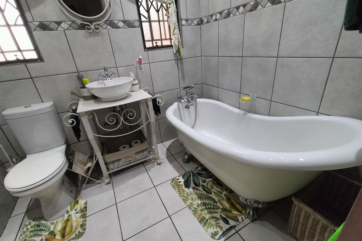 A well-maintained bathroom featuring a classic clawfoot bathtub, ceramic vessel sink, and neutral wall tiling with decorative border accents.