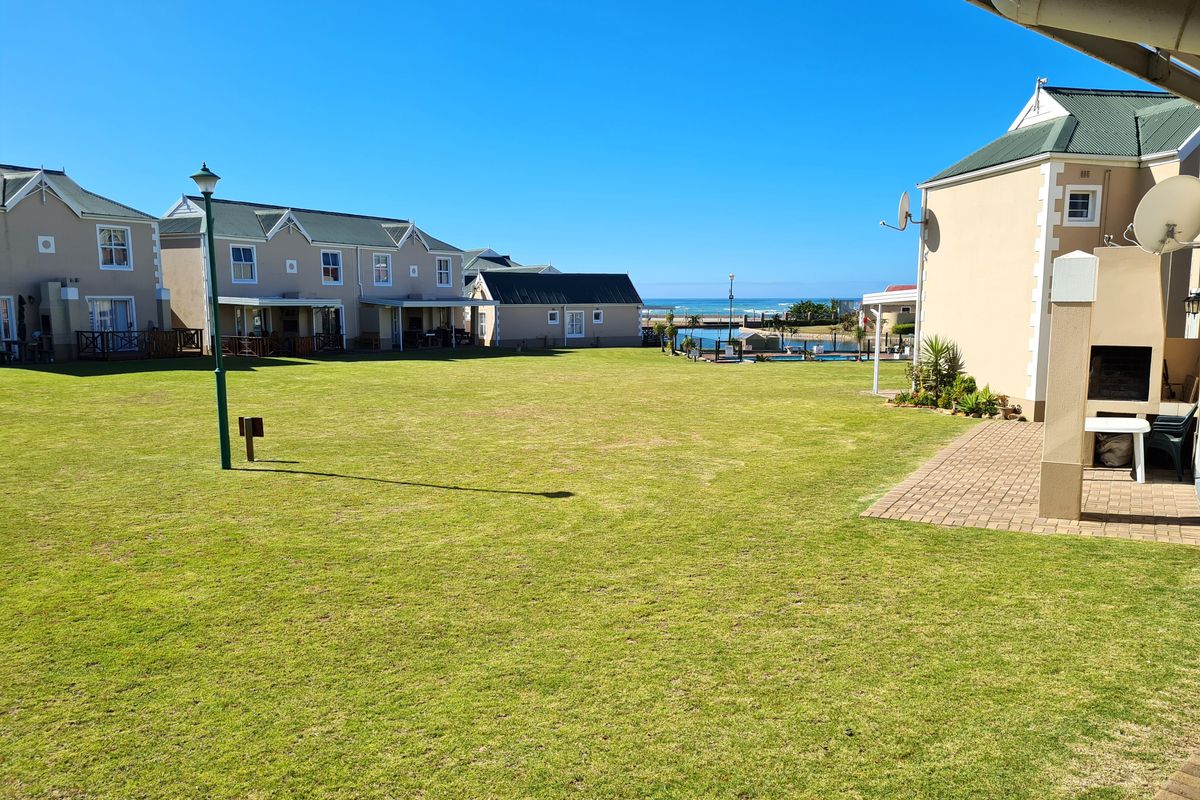 A spacious communal lawn area between townhouse units, featuring a built-in braai on the patio and a view towards the coast.