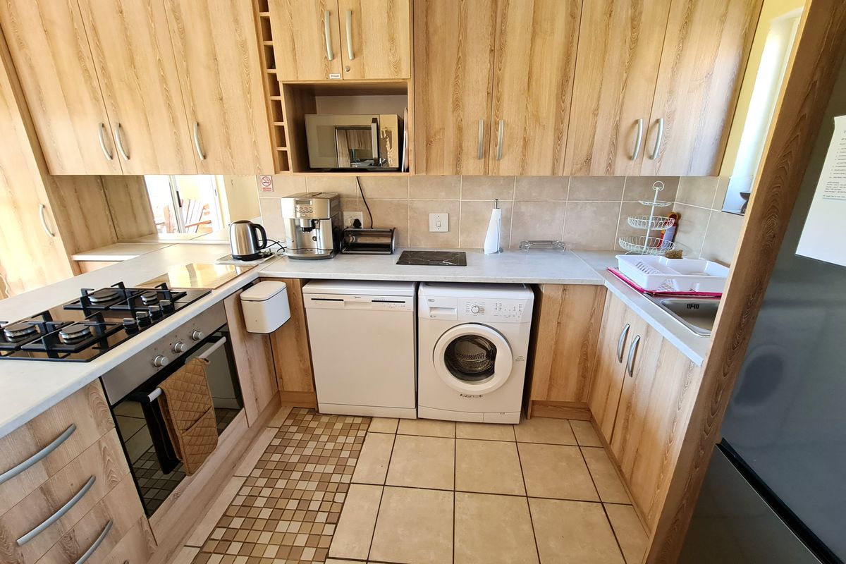 Functional kitchen featuring light wood-finish cabinetry, gas hob, built-in oven, and integrated microwave with tiled flooring and backsplash.