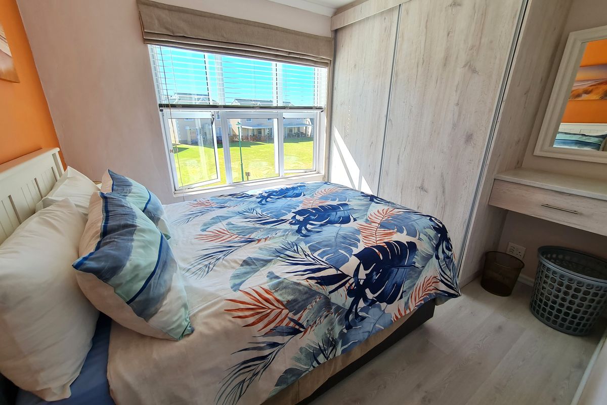 A well-maintained bedroom featuring light-toned laminate flooring, a built-in wardrobe, and a functional built-in vanity area with natural light.