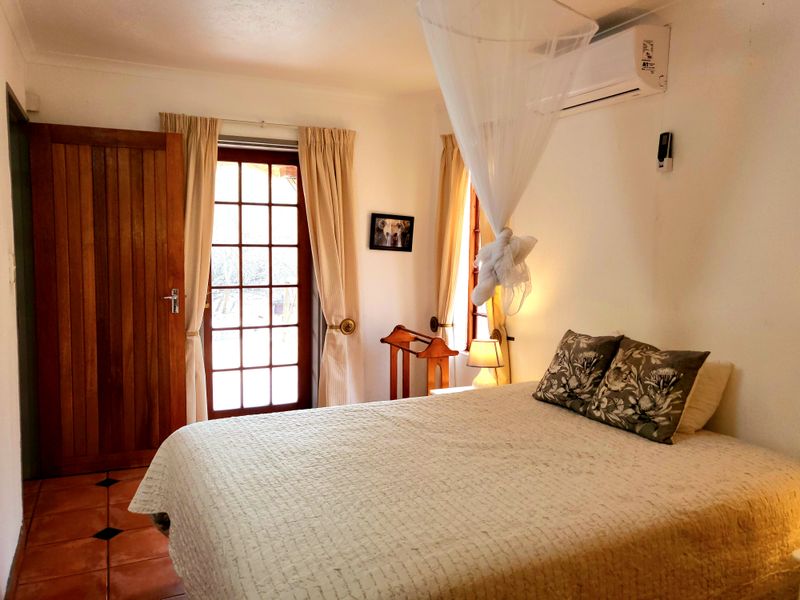 A cozy bedroom featuring terracotta floor tiles, a split-system air conditioner, and direct access to the outdoors through a wooden french door.