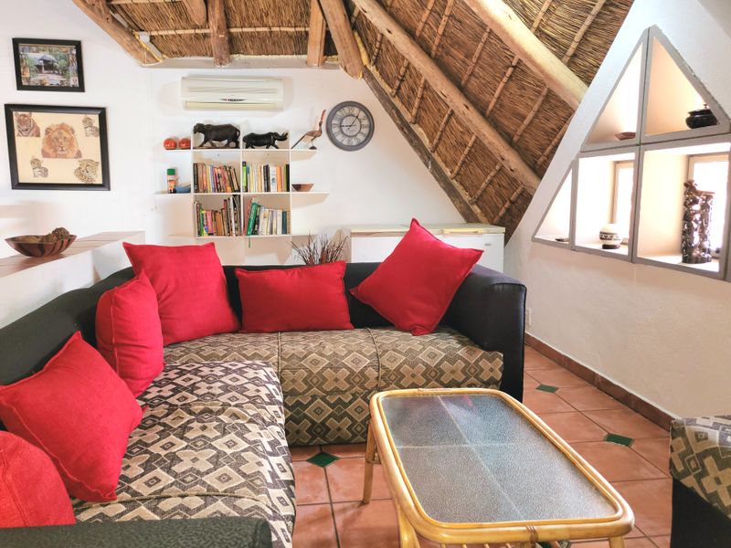 Cozy living area featuring a traditional thatched roof with exposed timber rafters, tiled flooring, and a unique triangular window design.