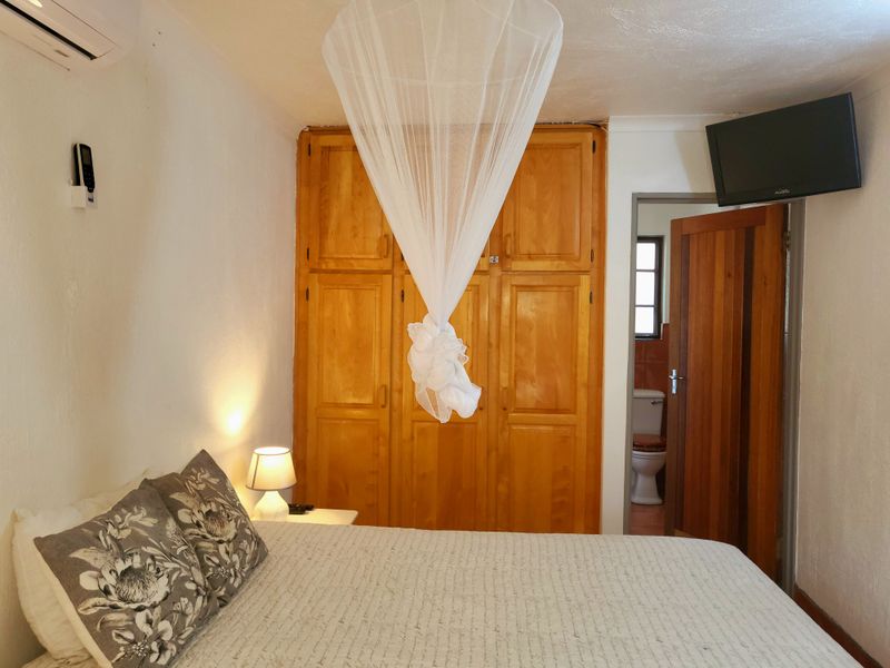 A bedroom featuring built-in wooden cabinetry, a wall-mounted air conditioning unit, and direct access to an en-suite bathroom.