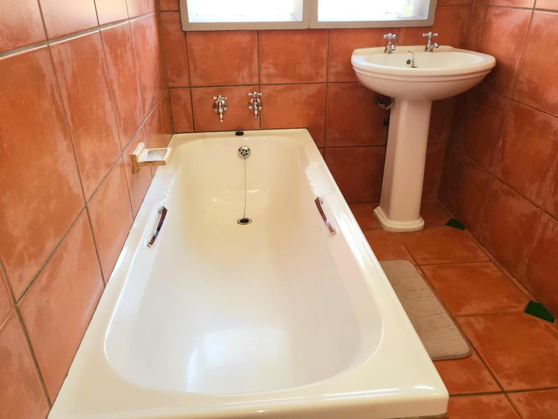 A functional bathroom featuring a white pedestal basin and a built-in bathtub, finished with terracotta-toned ceramic wall and floor tiles.