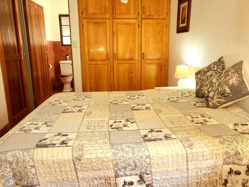 A bedroom featuring built-in wooden cupboards and an adjoining en-suite bathroom with tiled finishes.