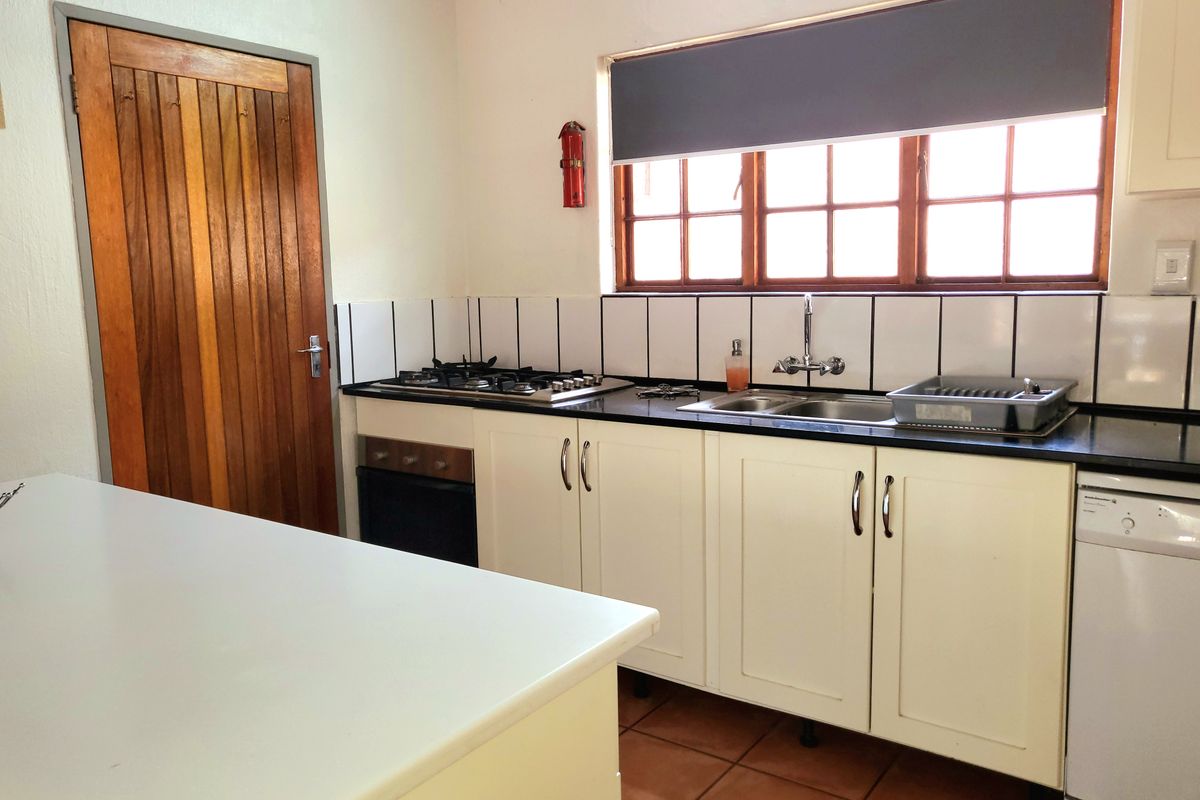 A functional kitchen featuring white cabinetry, dark countertops, a gas hob, built-in oven, and classic terracotta floor tiles.