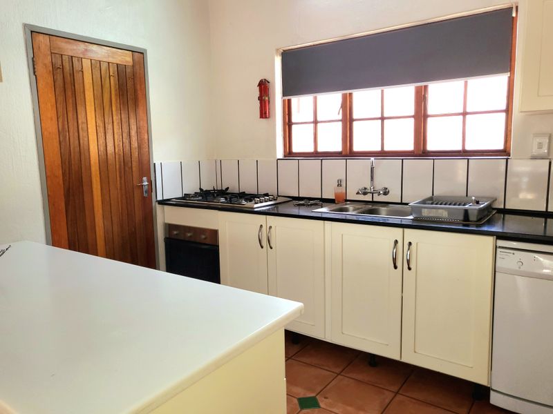 A functional kitchen featuring white cabinetry, dark countertops, a gas hob, built-in oven, and classic terracotta floor tiles.