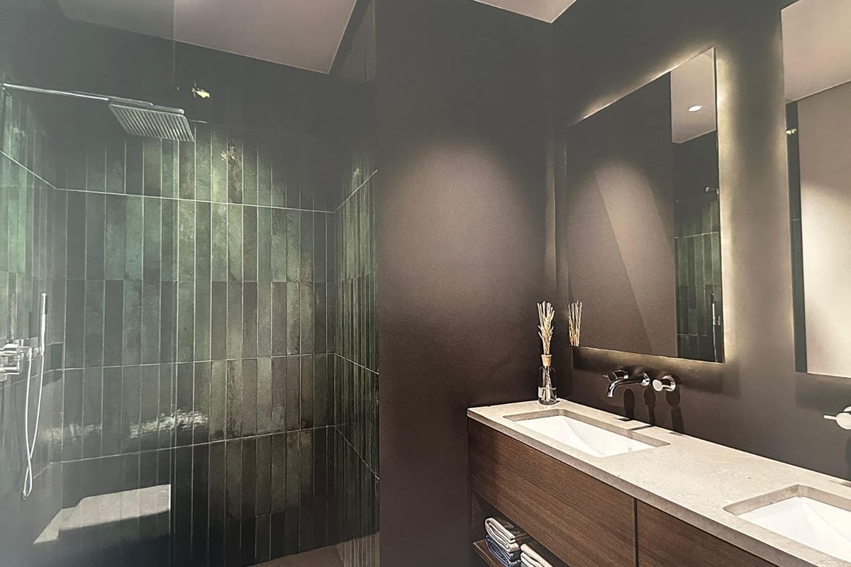 Modern bathroom featuring a walk-in shower with green subway tiles, a double vanity with integrated sinks, and a sleek backlit mirror.
