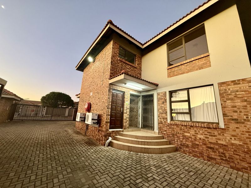 Front exterior view of a two-story face brick apartment building featuring a paved driveway, security gates, and external air conditioning units.
