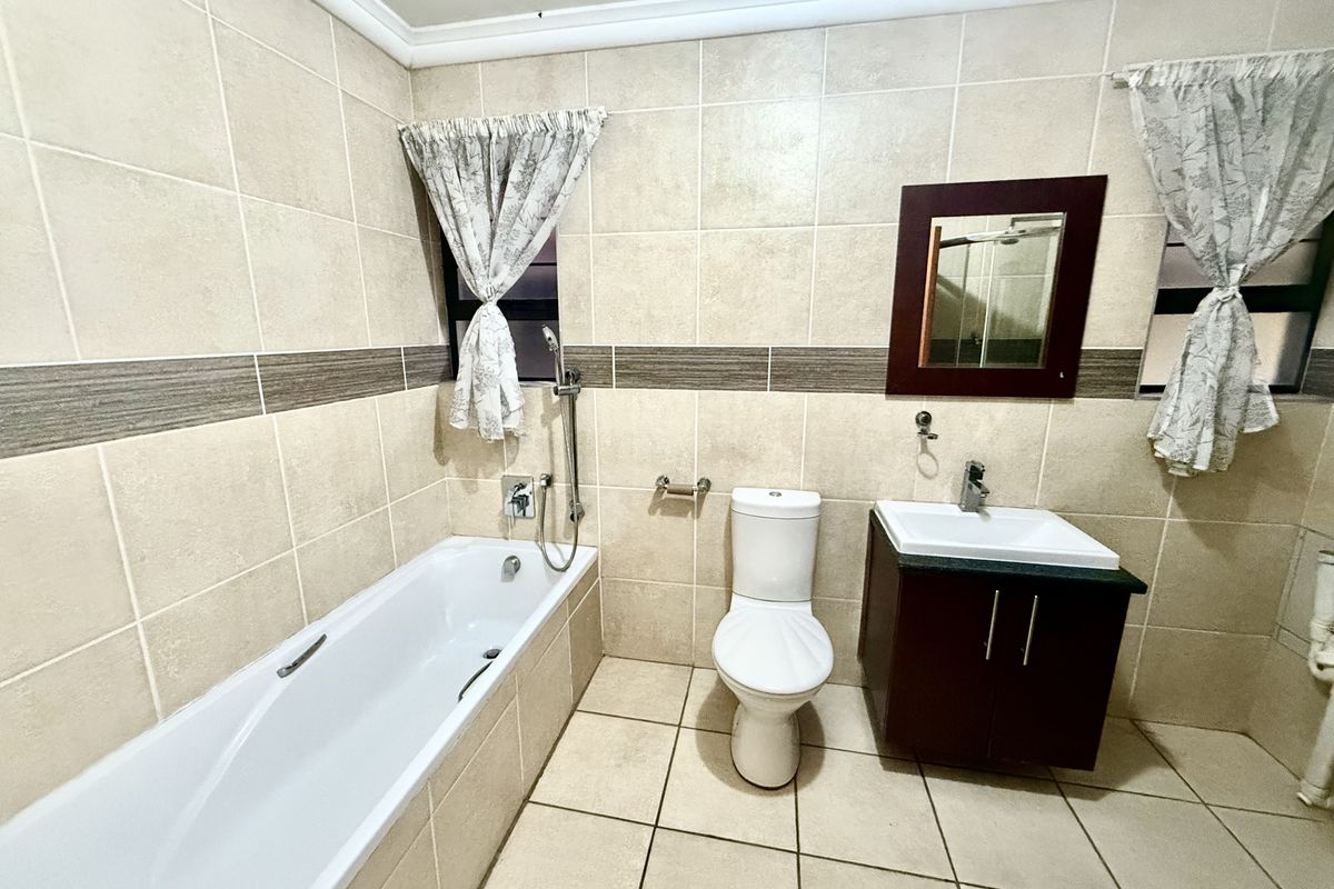 A functional bathroom featuring a built-in bathtub, a modern vanity with a washbasin, and neutral wall and floor tiling.