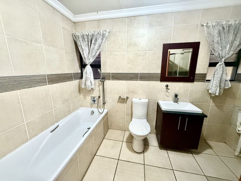 A functional bathroom featuring a built-in bathtub, a modern vanity with a washbasin, and neutral wall and floor tiling.